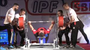 Powerlifter bench pressing with spotters nearby